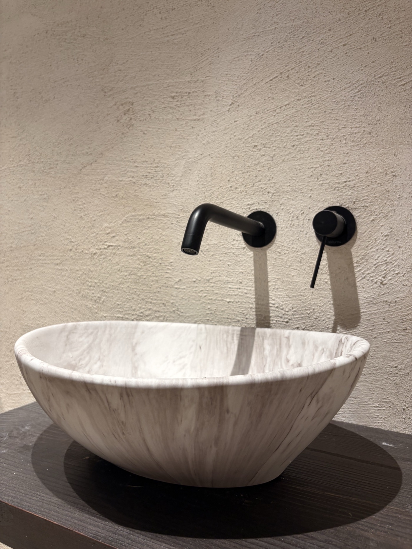 Lavabo de mármol con grifería negra sobre pared de cal